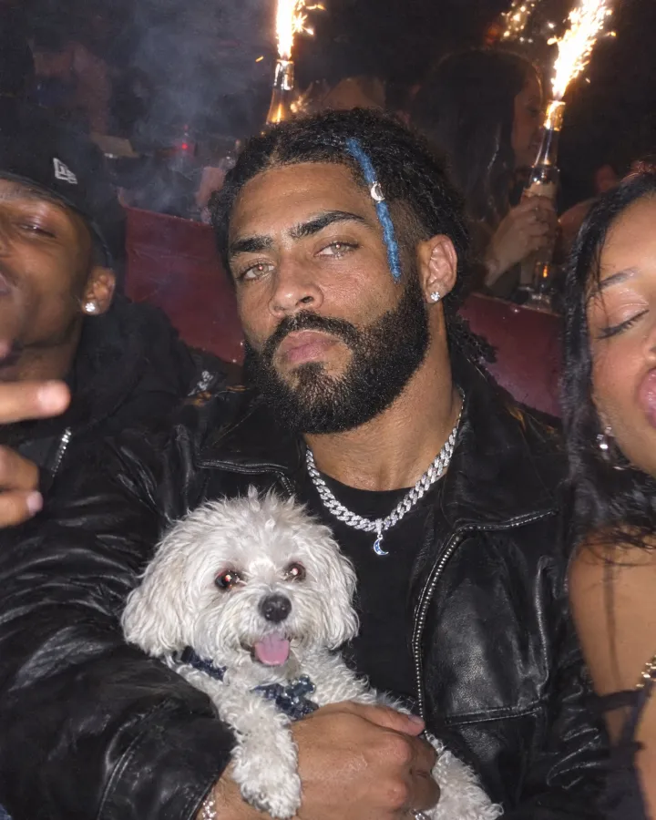 In a red club booth with friends, holding a small white fluffy dog, sparkler bottles burning behind.