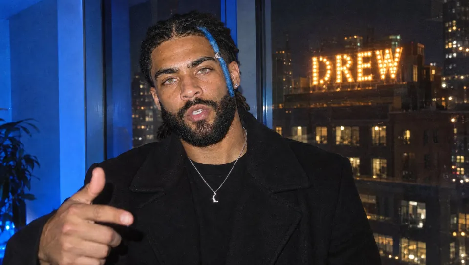 Rapping and pointing at the lens by a blue-lit window, his name in bulbs on a building across the street behind him.